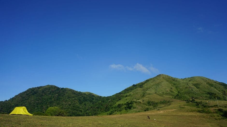 Experience the tranquil beauty of Nasugbu's green mountains with a sunlit campsite under a clear blue sky. (Photo by Jervine on Pexels)