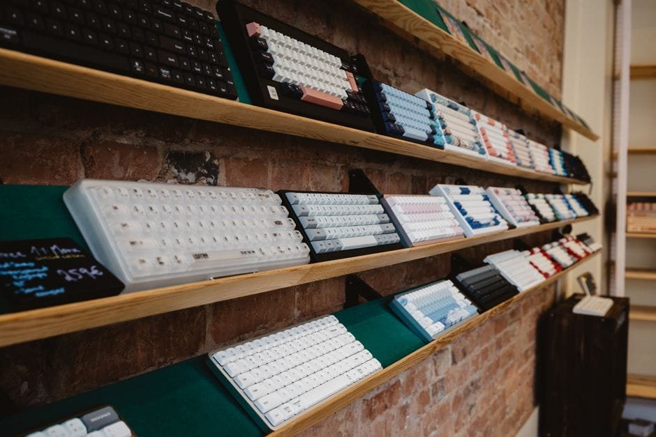 A variety of mechanical keyboards neatly displayed on a shelf in a brick-walled store interior. (Photo by Sebastian Luna on Pexels)