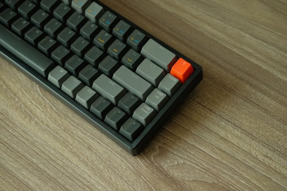 A detailed view of a mechanical keyboard with orange accent key on a wooden table. (Photo by An  Tran on Pexels)