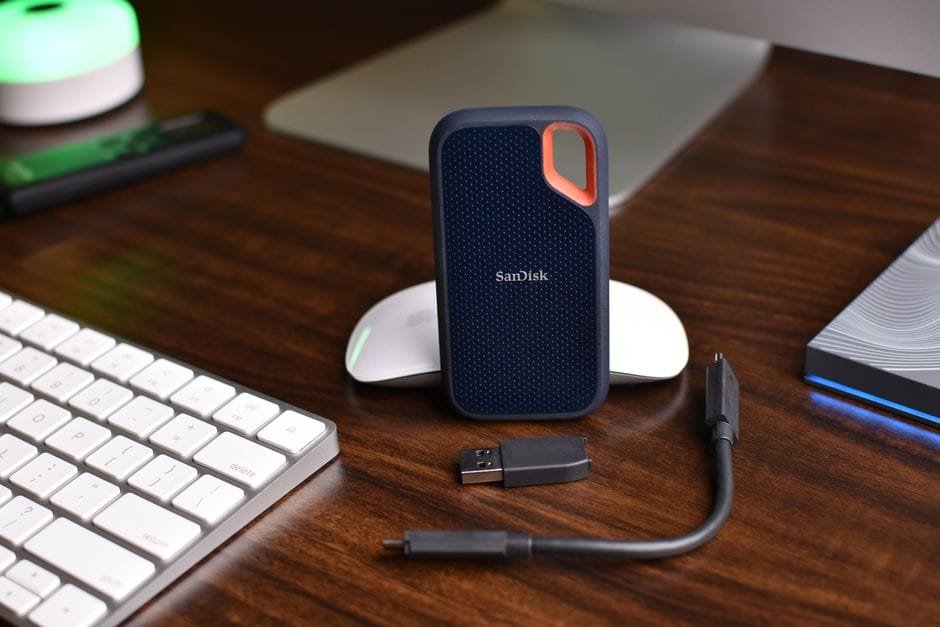 SanDisk portable SSD with USB cable and computer accessories on a wooden desk. (Photo by Avinash Kumar on Pexels)