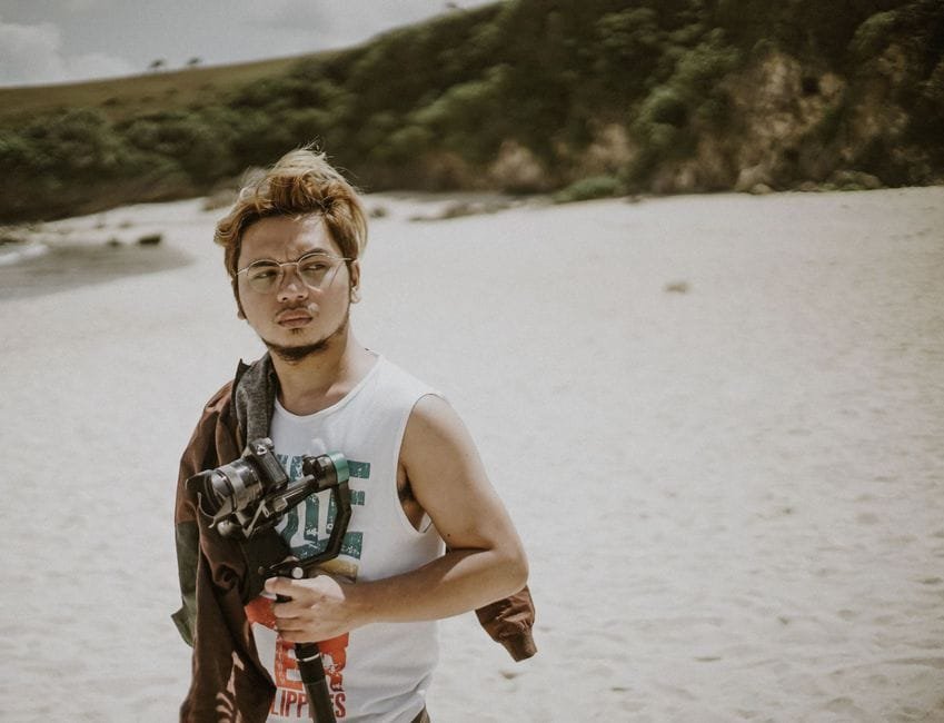Young man with camera on Basco beach, capturing the essence of photography amidst nature. (Photo by Kenneth Surillo on Pexels)
