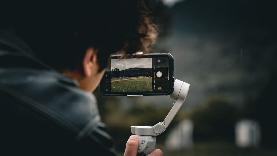 Person using a smartphone and gimbal to film a scenic outdoor landscape. (Photo by Muhammet Raşit Kaplan on Pexels)