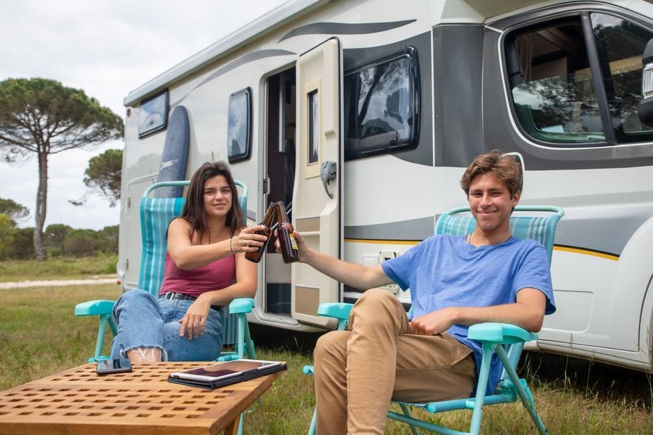 Happy couple clinking beer bottles outside camper during a relaxing vacation in Portugal. (Photo by Kampus Production on Pexels)