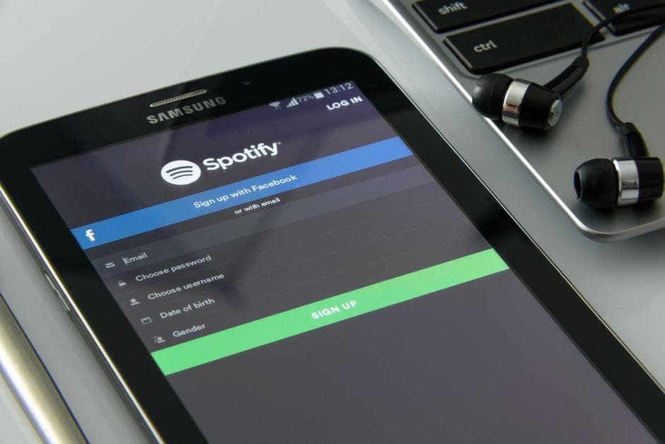 Smartphone showcasing Spotify login screen beside laptop and earphones on desk. (Photo by AS Photography on Pexels)