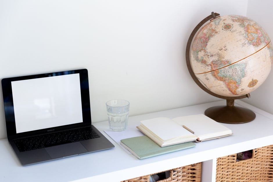 From above of empty screen of netbook placed near glass of water with opened white notepad near vintage globe at home (Photo by Tatiana Syrikova on Pexels)