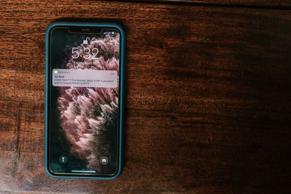 Close-up of smartphone on wooden surface displaying a bank alert message. (Photo by RDNE Stock project on Pexels)