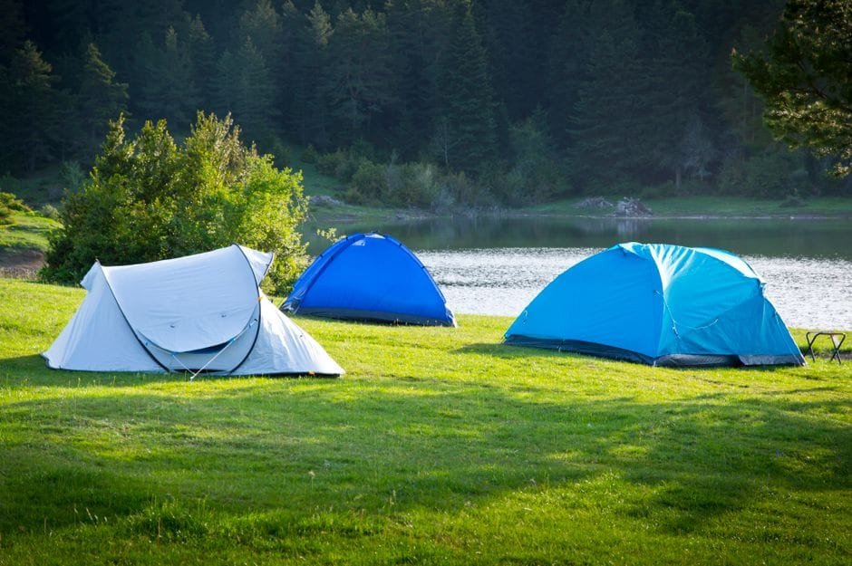 Serene campsite with tents by a forested lake, perfect for a summer outdoor adventure. (Photo by Adem Percem on Pexels)