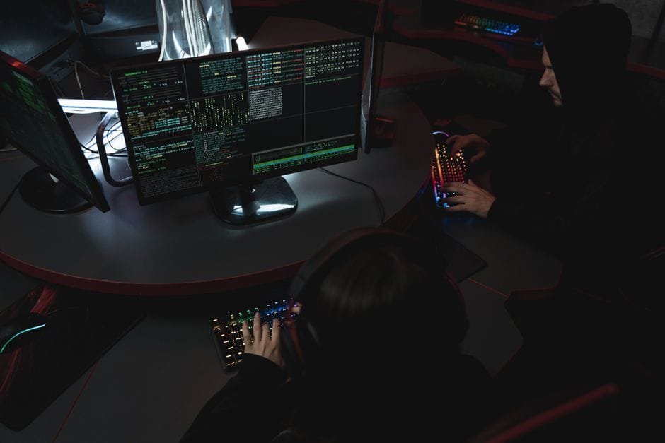 A group of people in a dark room working on computers, related to cybersecurity. (Photo by Tima Miroshnichenko on Pexels)