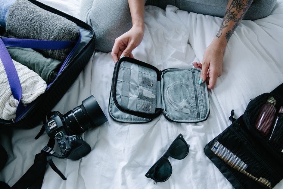 Traveler organizing essentials including a camera and packing cubes on a hotel bed. (Photo by Timur Weber on Pexels)