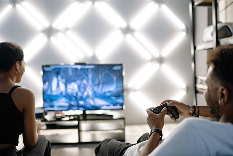 Two adults are having fun playing video games in a stylish, modern living room with LED lighting. (Photo by Yan Krukau on Pexels)