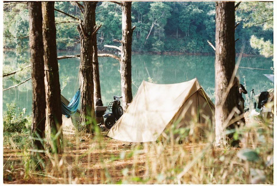 Tranquil camping scene with a tent and hammock in a forest near a lake. (Photo by Gin on Pexels)