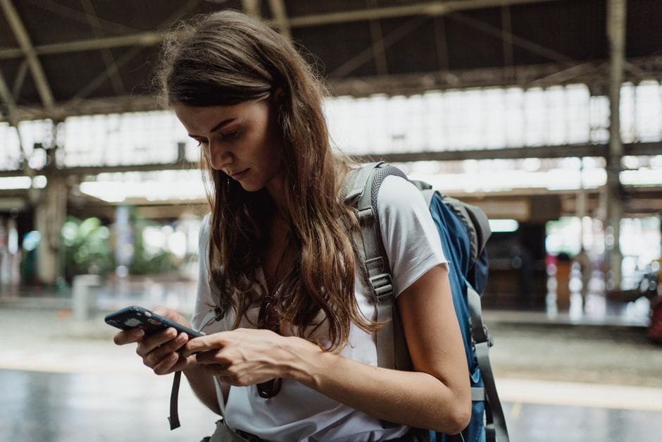 A young woman checks her smartphone while traveling at a train station. (Photo by Ketut Subiyanto on Pexels)