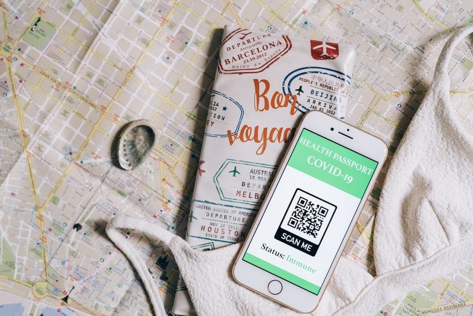 Smartphone displaying a health passport with QR code on a travel map and passport cover. (Photo by Leeloo The First on Pexels)
