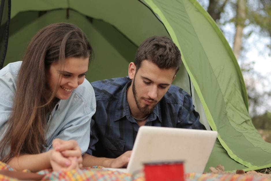 Happy couple resting in tent and surfing laptop while spending time together in park (Photo by Andrea Piacquadio on Pexels)