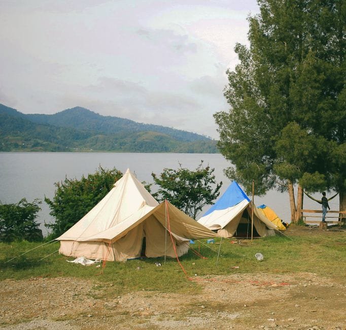 Peaceful lakefront camping scene with tents and mountains, ideal for nature and adventure seekers. (Photo by Padli Pradana on Pexels)