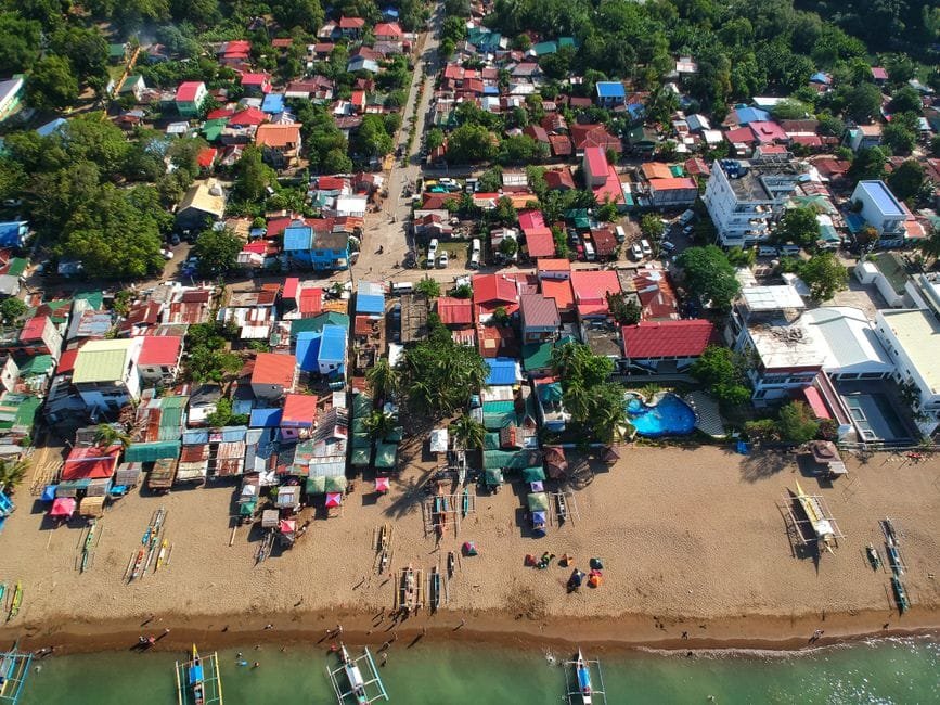 A vibrant aerial view of a coastal town in the Philippines, showcasing colorful rooftops, beachfront, and local boats. (Photo by Ferdie Cayanga on Pexels)