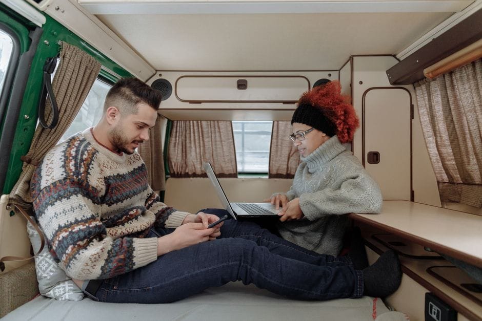 Couple using a smartphone and laptop inside a camper van, embracing the digital nomad lifestyle. (Photo by Thirdman on Pexels)