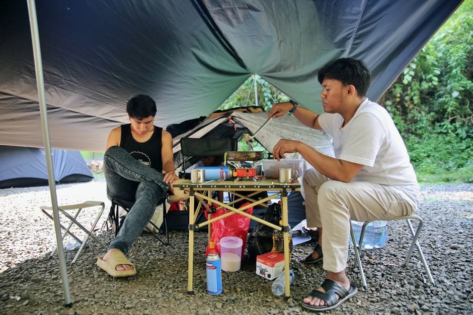 Two men enjoying an outdoor camping trip, preparing food under a tarp-covered area. (Photo by Heru Dharma on Pexels)