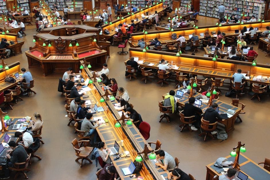 A lively university library scene with students studying diligently at wooden desks. (Photo by Pixabay on Pexels)