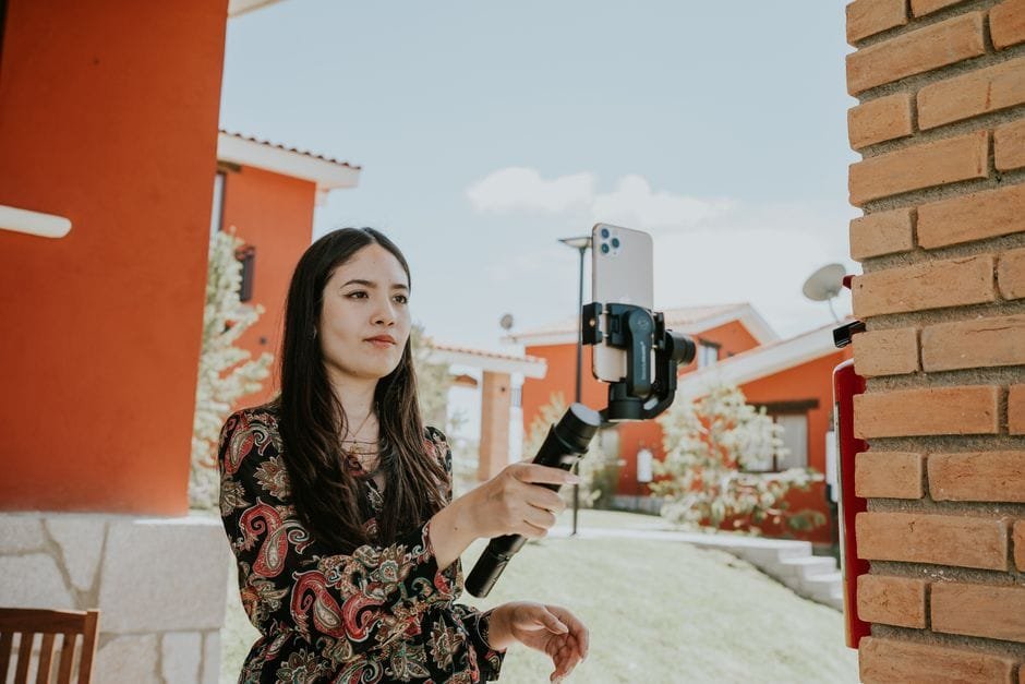 Young woman using a smartphone on a stabilizer for video recording outdoors. (Photo by Amar  Preciado on Pexels)