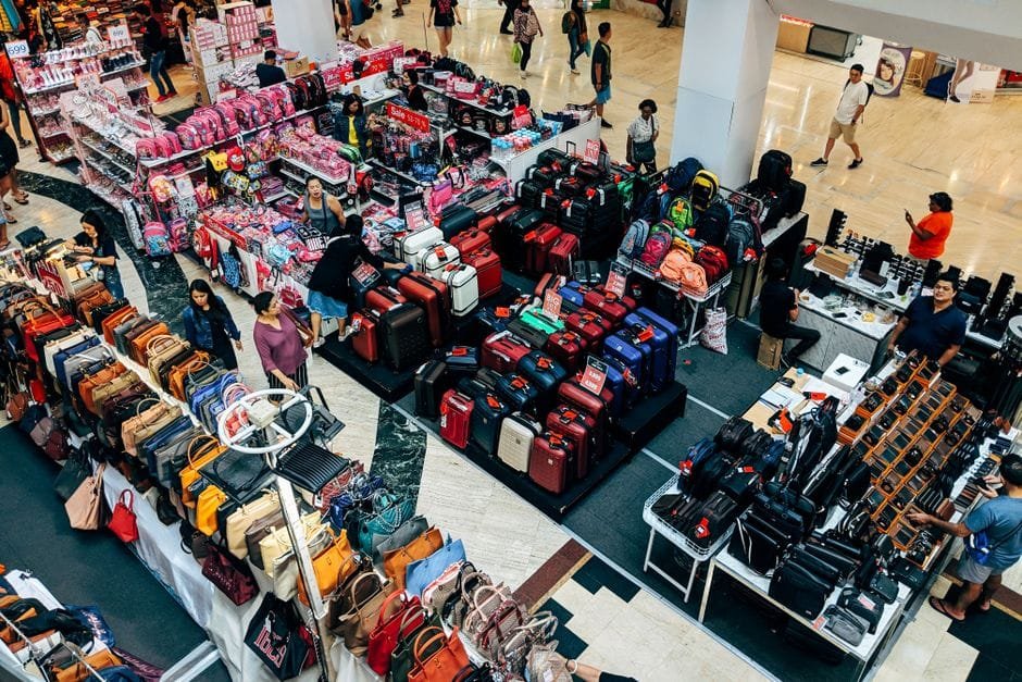 Overhead view of a vibrant shopping area in a Bangkok mall featuring purses, suitcases, and bustling shoppers. (Photo by Markus Winkler on Pexels)