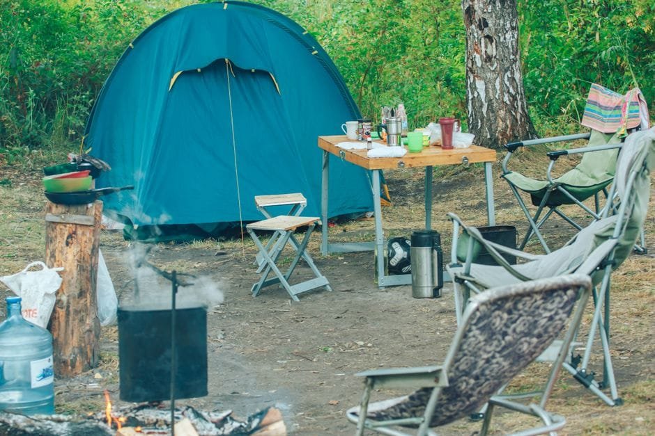 Serene campsite featuring a tent, chairs, and campfire amidst lush greenery for a perfect outdoor adventure. (Photo by Bulat Khamitov on Pexels)