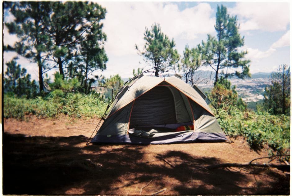 A tent pitched among trees on a sunny day, perfect for a summer camping adventure. (Photo by Minol Song on Pexels)