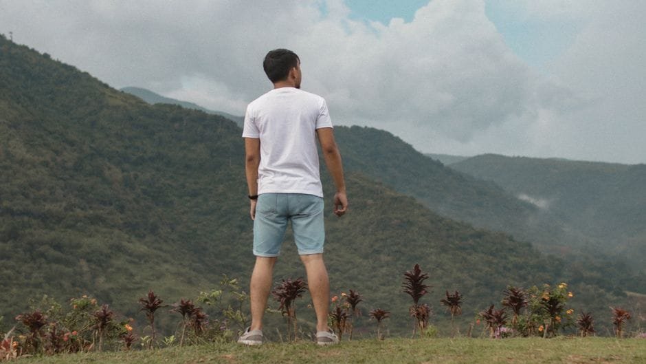 Man in casual attire standing on hill, observing lush Bacolod mountains. (Photo by Godwin Torres on Pexels)
