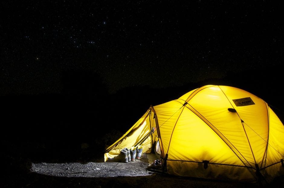 A glowing yellow tent pitched outdoors under a vast, star-filled night sky, capturing the essence of camping adventure. (Photo by Pixabay on Pexels)