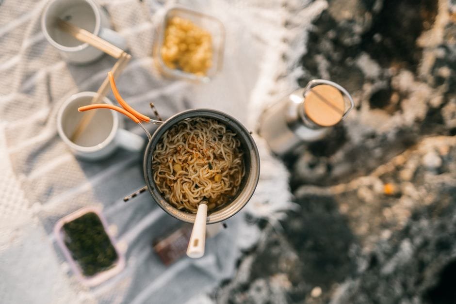 Top view of instant noodles cooking during a camping trip, with various outdoor kitchen essentials. (Photo by Taryn Elliott on Pexels)
