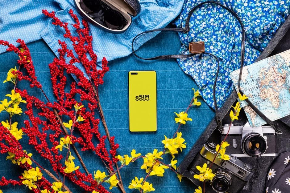 Flat lay of travel essentials including smartphone, camera, and vibrant flowers on a colorful background. (Photo by Jacob on Pexels)