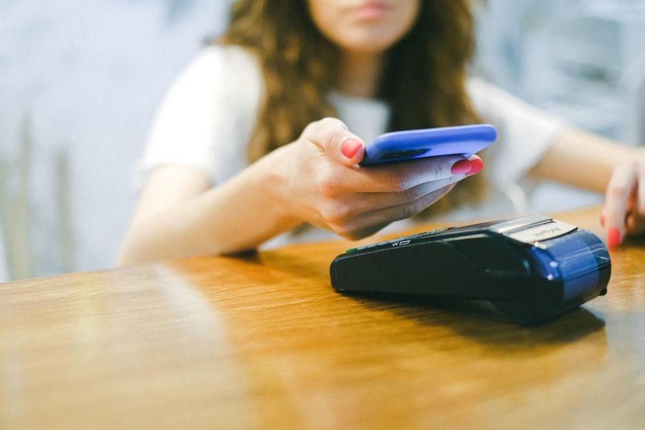 A woman processes a contactless payment using her smartphone at a payment terminal. (Photo by Anna Shvets on Pexels)