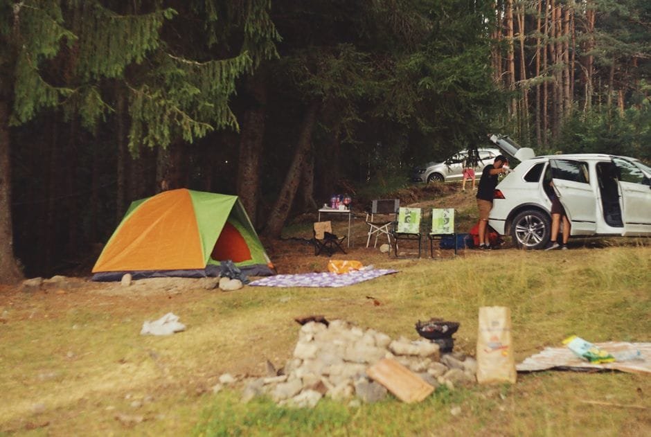 Explore a peaceful camping scene in the forest with a tent, car, and campfire setup. (Photo by Simeon Stoilov on Pexels)
