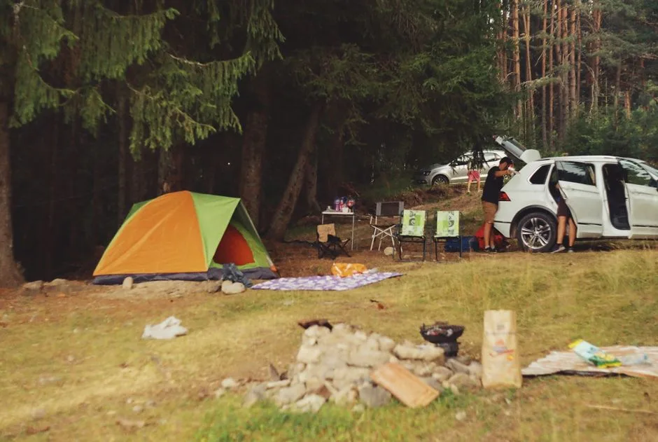 Explore a peaceful camping scene in the forest with a tent, car, and campfire setup. (Photo by Simeon Stoilov on Pexels)