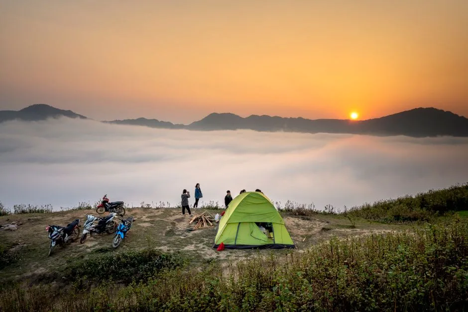 A scenic view of camping at sunrise with a tent and motorcycles overlooking fog-covered mountains. (Photo by Quang Nguyen Vinh on Pexels)