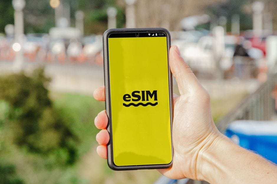 A person holds a smartphone featuring an eSIM display against an outdoor urban backdrop. (Photo by Jacob on Pexels)