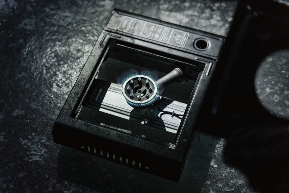 Detailed view of a portable stove with a lit blue flame on a textured surface. (Photo by Tima Miroshnichenko on Pexels)