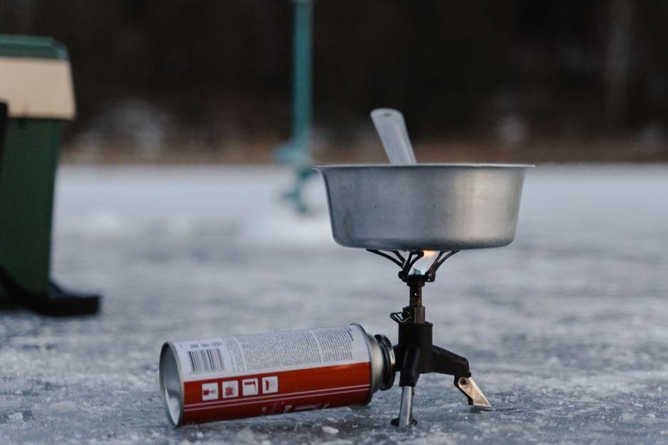 A camping stove setup on ice including a pot and butane canister for winter outdoor cooking. (Photo by Tima Miroshnichenko on Pexels)
